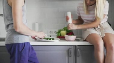 Sevgi dolu çift birlikte sebze kesiyor, mutfakta öğle yemeği için salataya baharat ekliyor.