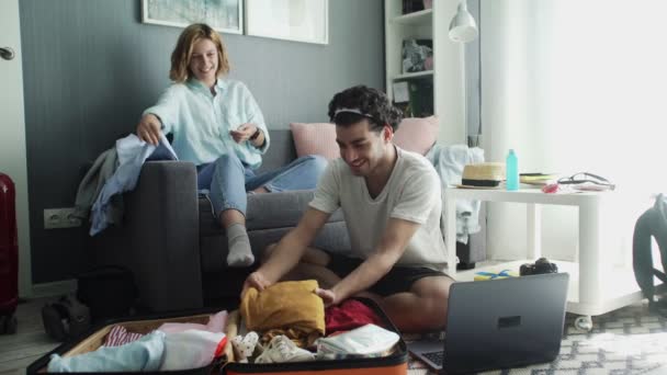 Sonrisa pareja recoge ropa para viajar al extranjero sentado en el sofá y hablando — Vídeos de Stock