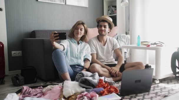 Giovane coppia che fa selfie con valigia e vestiti sullo sfondo. Prepararsi per le vacanze estive — Video Stock
