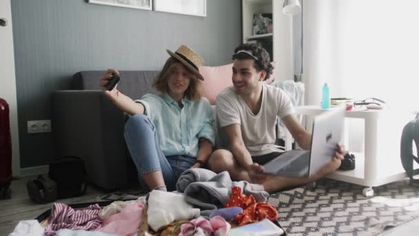 Una ragazza con un cappello e un ragazzo con un portatile registrare video al telefono prima di viaggiare — Video Stock
