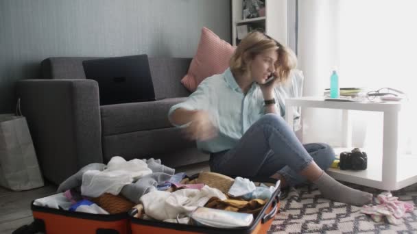 Young woman packing suitcase in home, getting ready for road trip, preparing luggage and talking on smartphone — Stock Video