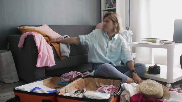 Triest meisje gooit kleren uit een koffer — Stockvideo