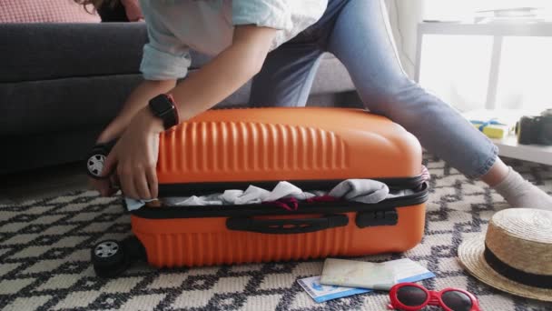 Femme mignonne debout sur ses genoux sur une valise orange surchargée et essayant de la fermer — Video