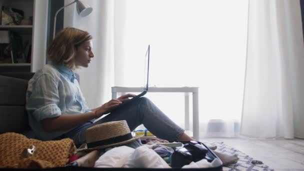 Menina perto de uma mala para férias funciona em um laptop — Vídeo de Stock