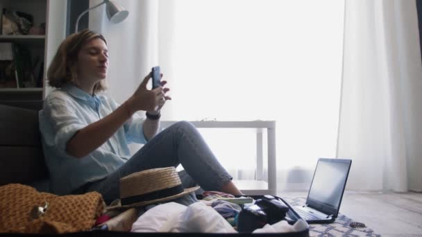 Mladá žena sedí na podlaze v blízkosti otevřeného kufru a bere selfie — Stock video