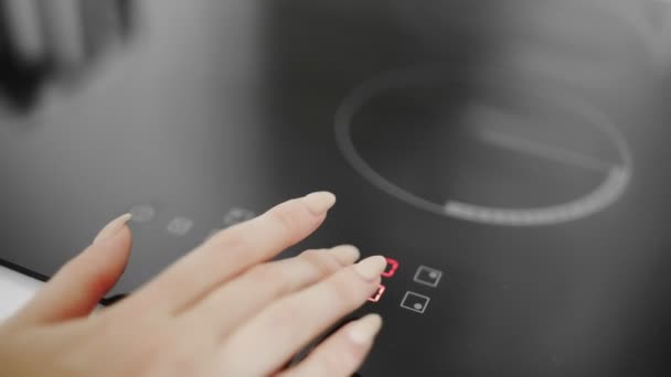 Primer plano de una mano femenina encendida en la cocina de inducción — Vídeo de stock