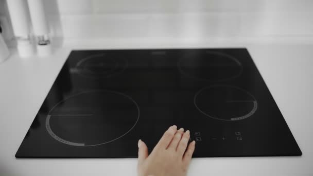 Primer plano de una mano femenina encendida en la cocina de inducción — Vídeo de stock