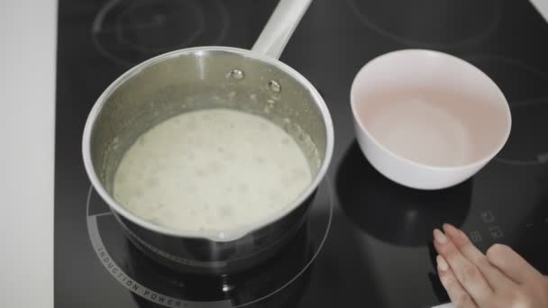 Harina de avena con los cocineros de leche y hierve en una cacerola de metal en la cocina estufa — Vídeos de Stock