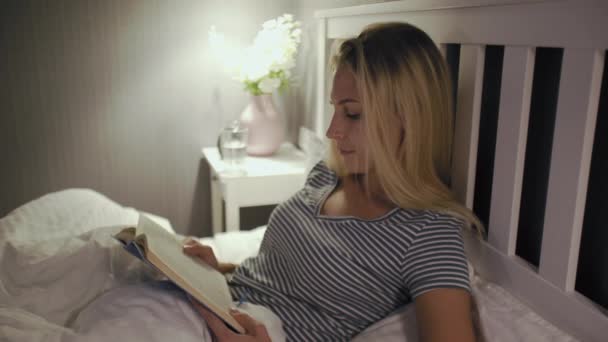 Женщина в ночном белье читает книгу перед сном — стоковое видео