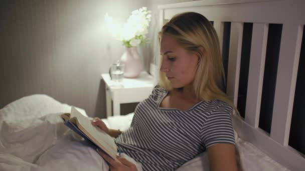 Жінка в нічній білизні закінчила читати книгу і йде спати — стокове відео