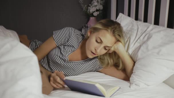 Chica joven acostada en la cama y leyendo un libro en su tiempo libre — Vídeos de Stock