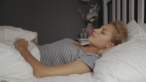 Jonge vrouw die 's nachts in bed ligt. Mooi blond slapend meisje. Vrouw heeft een nare droom. — Stockvideo