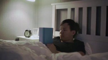 Genç adam yatakta uzanıp kitap okuyor ve sonra uykuya dalıyor.