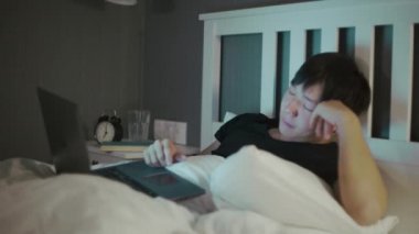 Genç Asyalı adam dizüstü bilgisayar kullanmayı bitirdi ve uyumaya gitti.