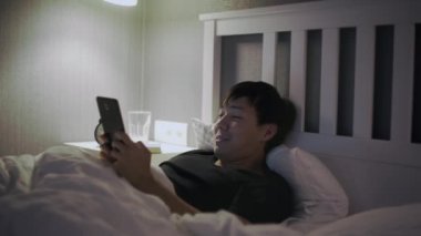 Tablet bilgisayarlı genç Asyalı adam yatakta yatıyor.