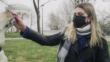 Siyah maskeli bir kadın, karantina Coronavirus COVID-19 pandemisi sırasında labrador köpeğiyle parkta oynuyor.