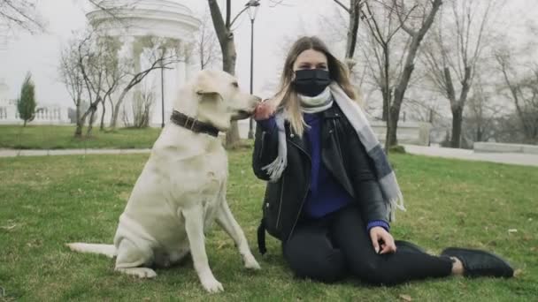 Женщина сидит на земле и играет со своей собакой-лабрадором в парке во время пандемии коронавируса COVID-19 — стоковое видео