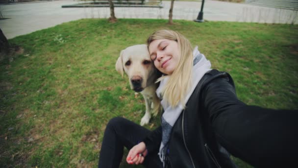 Joven mujer rubia sonriente tomando selfie con perro labrador retriever en el parque — Vídeo de stock