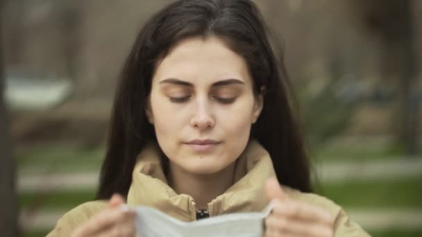 A mulher coloca uma máscara para proteção contra o coronavírus COVID-19. Retrato de uma menina usando uma máscara protetora ao ar livre — Vídeo de Stock