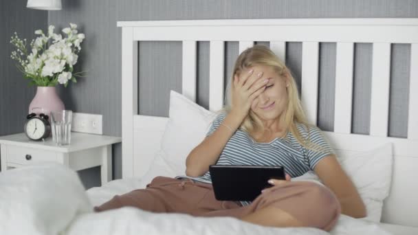 Jeune femme heureuse regardant une vidéo drôle sur une tablette couchée sur un lit à la maison — Video