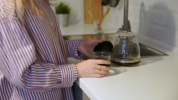 Genç bir kadın mutfağa gitmek için tekrar kullanılabilir fincana kahve koyuyor. — Stok video