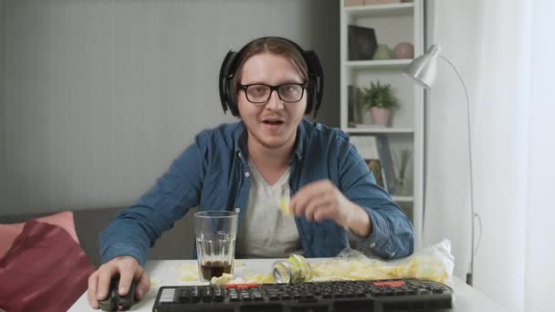 Jovem concentrado jogando videogame, comendo batatas fritas e bebendo cola — Vídeo de Stock