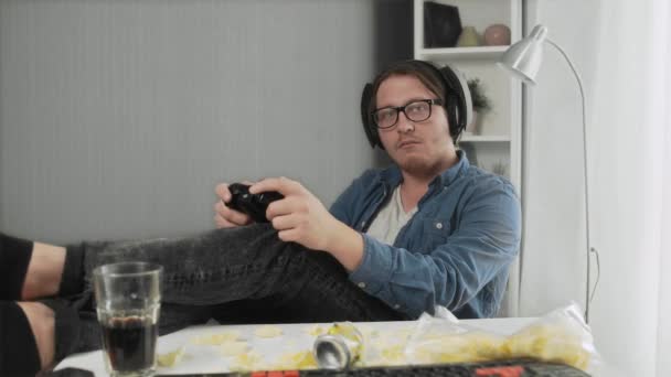 Молодой человек сидит на диване и играет в видеоигры . — стоковое видео