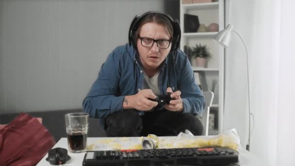 Un uomo si siede in posa divertente e gioca, tiene in mano un joystick . — Video Stock