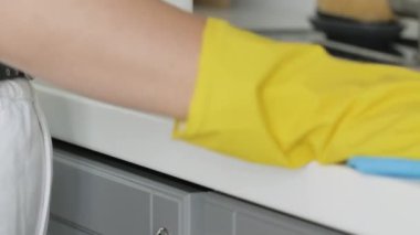 Sarı eldivenli ev kadını masayı mavi bez ve deterjanla yıkıyor..