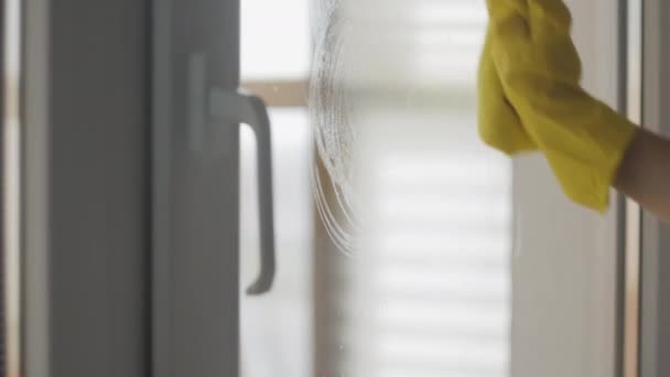 Hausfrau in gelben Handschuhen wäscht Fenster mit gelbem Lappen und Waschmittel. — Stockvideo
