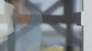 Sarı eldivenli genç bir kadın camları beyaz bez ve deterjanla yıkıyor..