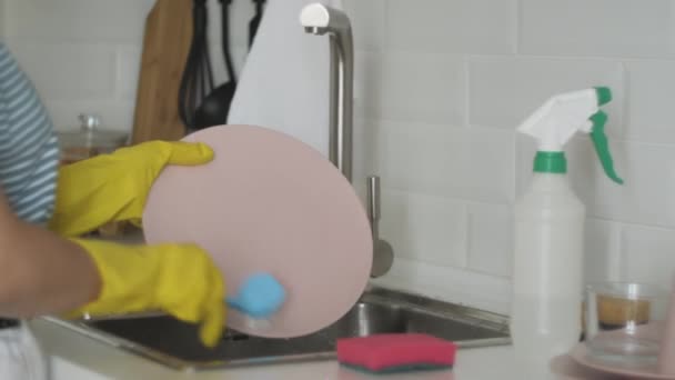 Молодая женщина в перчатках моет посуду на кухне — стоковое видео