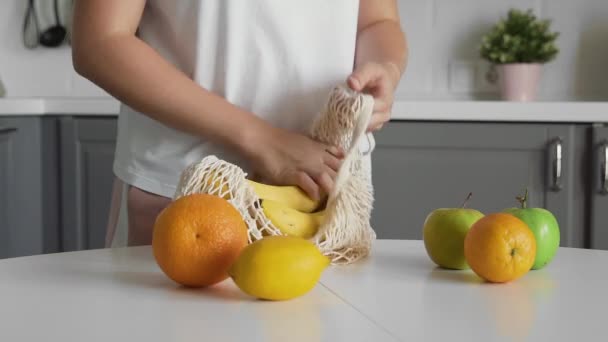 Närbild av ung kvinna sätter apelsiner bananer äpplen i en transparent eko väska. Noll avfallskoncept. Inget plastliv. Hälsosam fitness livsstil. Begreppsåtervinning. — Stockvideo