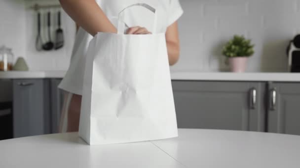Närbild av ung kvinna packa upp shoppingväska med grönsaker på köket på träbord. Noll avfall hem och eko väska. Ekologisk handel. — Stockvideo