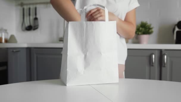 Großaufnahme einer jungen Frau, die auf dem Holztisch in der Küche eine Einkaufstasche mit Gemüse auspackt. Zero waste home und eco bag. Öko-Einkauf. — Stockvideo