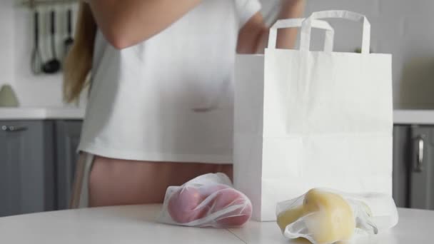 Close up de mulher jovem embalagem saco de compras com legumes na cozinha em mesa de madeira. Sem desperdício em casa e saco ecológico. Eco compras . — Vídeo de Stock