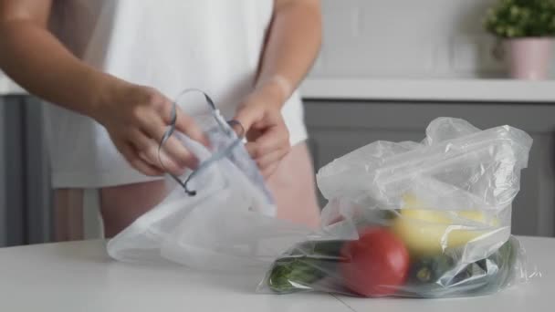 Close up of Young woman move vegetables from plastic bag to reusable mesh bag on the kitchen wooden table. Zero waste home and eco bag. Eco Shopping. — Stock Video