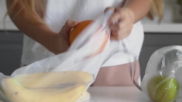 Close-up van jonge vrouw verplaatsen vruchten van plastic zak naar herbruikbare mesh zak op de houten keukentafel. Geen afval thuis en eco tas. Eco-winkelen. — Stockvideo