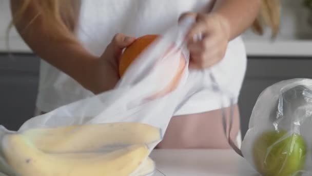 Gros plan de la jeune femme déplacer les fruits du sac en plastique au sac en maille réutilisable sur la table en bois de la cuisine. Zéro déchet maison et sac écologique. Eco Shopping . — Video