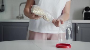 Kadın yulaf ezmesini depolamak için cam kavanoza doldurur..