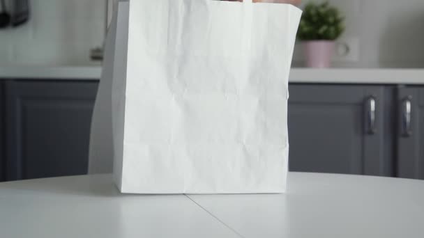 Zblízka žena vybaluje nákupní tašku s chlebem, ovesnou kaší, mlékem, zeleninou na dřevěném stole. Nulový plýtvání domů a eko taška. Eco Shopping. — Stock video