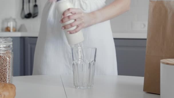 Gros plan de femme méconnaissable en robe blanche verse du lait de bouteille vintage au verre sur la table pour le petit déjeuner — Video