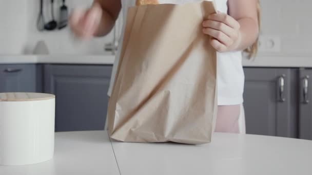 在厨房的木制桌子上，妇女打开装有面包、牛奶和橙子的购物袋。零浪费的家和生态袋。环保购物. — 图库视频影像