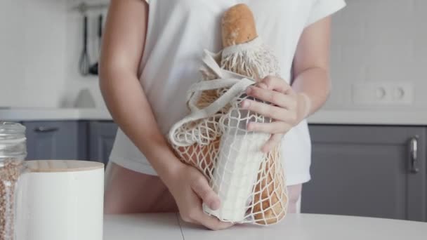 Женщина распаковывает на кухне на деревянном столе сумку с хлебом, молоком и апельсинами. Нулевые потери дома и экологическая сумка. Эко-шоппинг . — стоковое видео