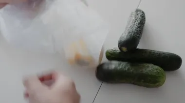 Mutfakta ahşap masanın üzerinde salatalık, domates ve biber bulunan alışveriş poşetlerini açan bir kadın. Sıfır atık ev ve çevre torbası. Çevre Alışverişi.