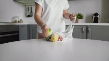 Sıfır atık ev ve çevre torbası. Eko-alışveriş. Mutfakta ahşap masanın üzerinde salatalık, domates ve biber bulunan yeniden kullanılabilir market poşetleri.