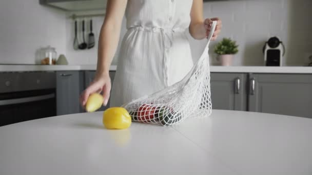 Vrouw stapt uit komkommers, tomaten, paprika 's op de keuken op houten tafel uit katoenen boodschappentas. Geen afval thuis en eco tas. Eco-winkelen. — Stockvideo