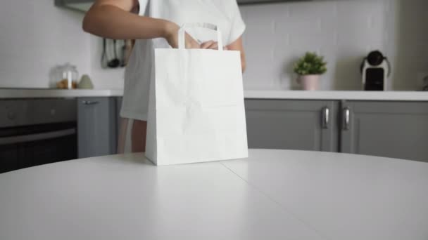 Mladá žena vybaluje nákupní tašku se zeleninou v kuchyni na dřevěném stole. Nulový plýtvání domů a eko taška. Eco Shopping. — Stock video