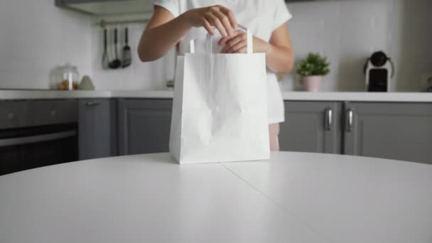 Młoda kobieta rozpakowuje torbę z warzywami w kuchni na drewnianym stole. Zero odpadów w domu i eko-torba. Zakupy ekologiczne. — Wideo stockowe