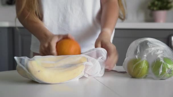 Närbild av ung kvinna flytta frukter från plastpåse till återanvändbara mesh väska på köksbordet. Noll avfall hem och eko väska. Ekologisk handel. — Stockvideo